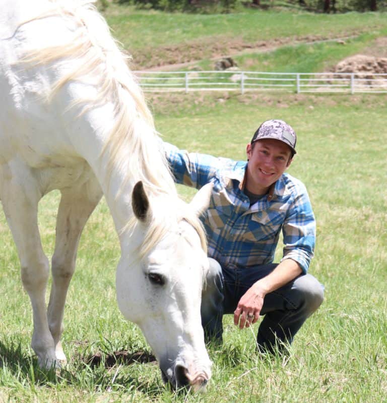 Young man with a white horse on a green pasture at Renewing Hope Ranch.
