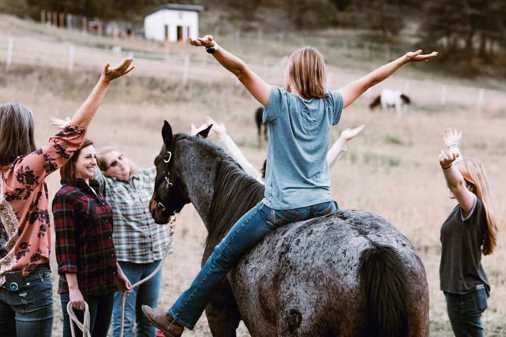Girl riding a horse with arms outstretched during equine experience at ranch.